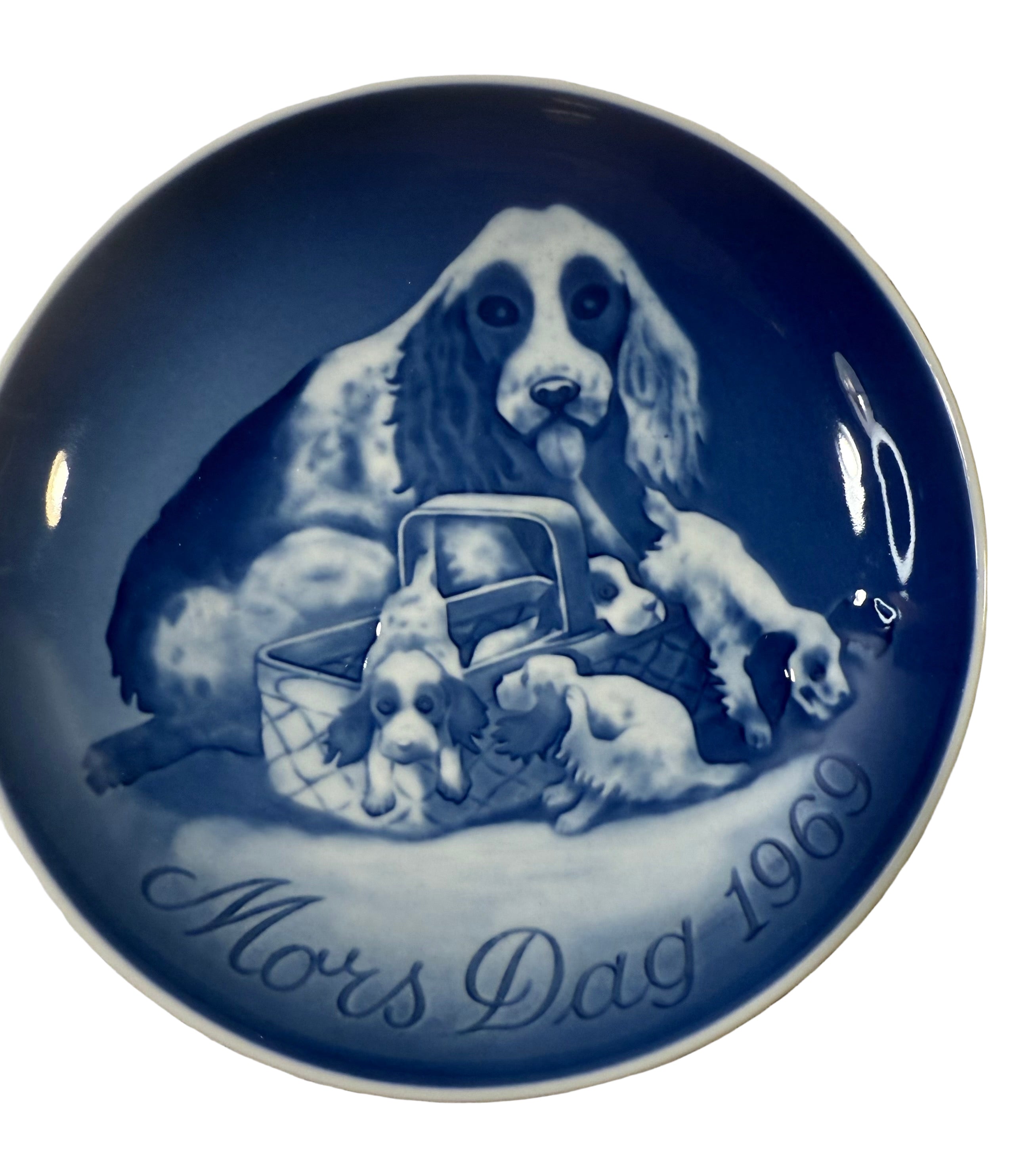 Blue ceramic plate with a dog and puppies design and 'Mors Dag 1969' text on a textured surface.