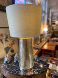Table lamp with a textured beige shade and metallic base on a marble surface.